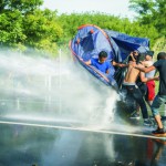 Migranti sa chránia stanom pred zásahom maďarských policajtov vodným delom počas zrážok na maďarsko -srbskej hranici Horgoš 2 pri obci Horgoš 16. septembra 2015. Migranti na srbskej strane hraníc pri juhomaďarskej obci Röszke v stredu popoludní stratili trpezlivosť, prerazili plot a začali utekať na maďarskú stranu. Príslušníci zásahovej jednotky maďarskej polície proti nim použili slzotvorný plyn a nasadili aj vodné delo